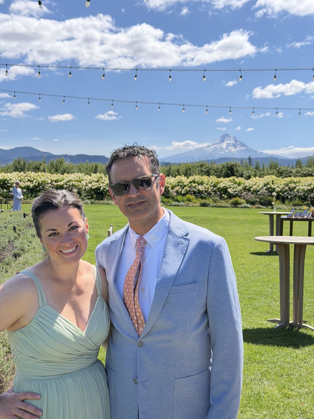 Jake and Salena dressed up on a sunny lawn with Mount Hood behind them